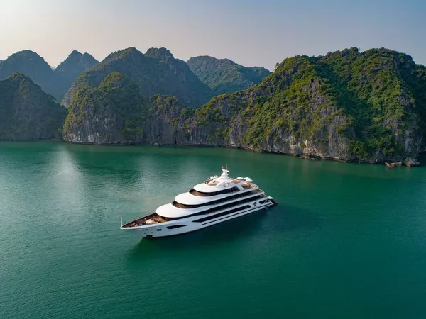 White luxury cruise ship on calm emerald water in Halong Bay, passing towering limestone karsts as it glides through the bay