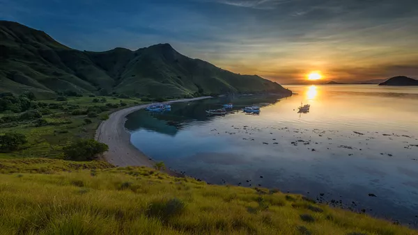 Sunset panorama of phinisi boats anchored along a sandy bay on a shared Komodo Islands trip, Labuan Bajo