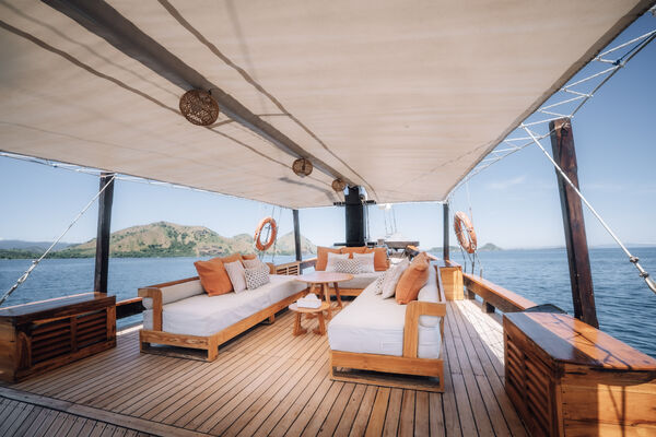 Sun deck with wooden daybeds and curtains on a phinisi boat, with open-water views on a Komodo cruise from Labuan Bajo