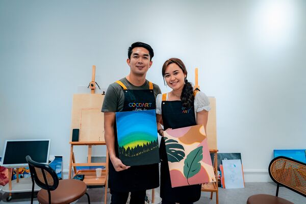 Smiling couple holding their finished canvases at CocoArt SG in Singapore during a private guided art jamming session