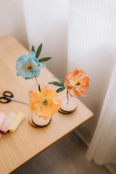 Orange and blue lifelike paper flowers in mini vases on a worktable in Singapore, set up for Flowers By Four workshops in Singapore