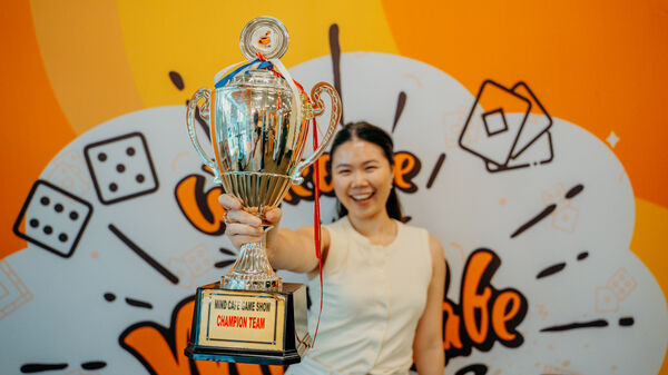 The Mind Cafe champion at Singapore raises a glass trophy in front of the 'Game Show' board-game mural, beaming