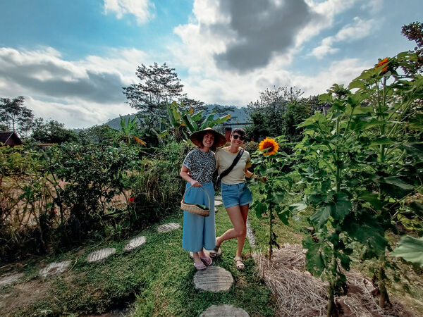 Two travellers posing on stepping stones through a vegetable garden with yellow flowers in Sidemen, Bali during a vegan cooking class