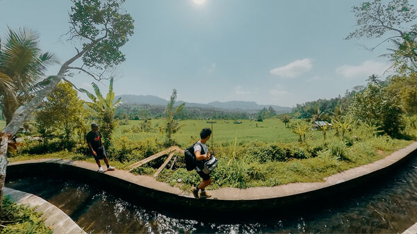 Backpackers walking alongside an infinity pool with lush fields and mountains in the distance in Bali under bright daylight