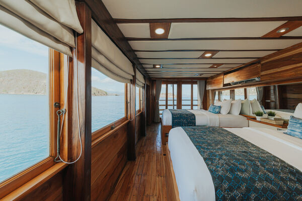 Long phinisi cabin interior with made-up beds, wooden rails and ocean-side views, designed for a Labuan Bajo 3D2N Komodo trip