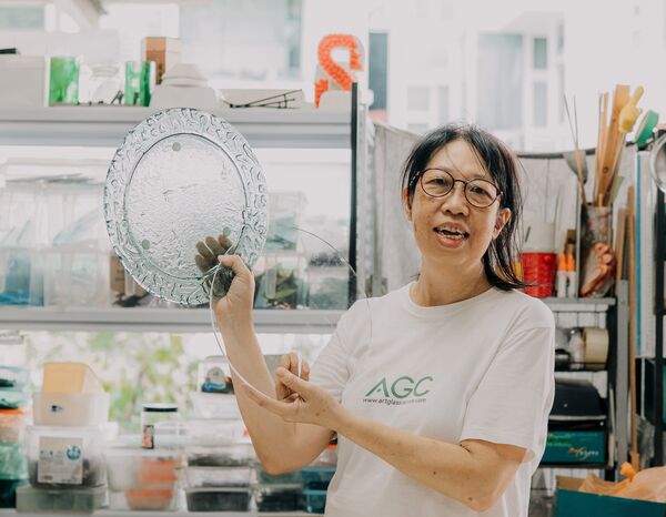 Tan Sock Fong holding a textured round glass piece at Art Glass Centre in Singapore, showing centrepiece skills—workshops in Singapore