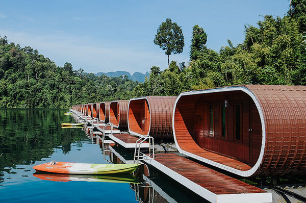 Wooden houseboat with an orange kayak moored at the pier on a still lake for a Khao Sok cruise at Cheow Lan Lake
