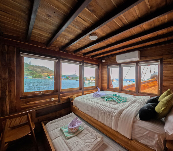 Archipelago Reserve twin beds in a wooden cabin with panoramic water windows during a Komodo liveaboard stay in Labuan Bajo