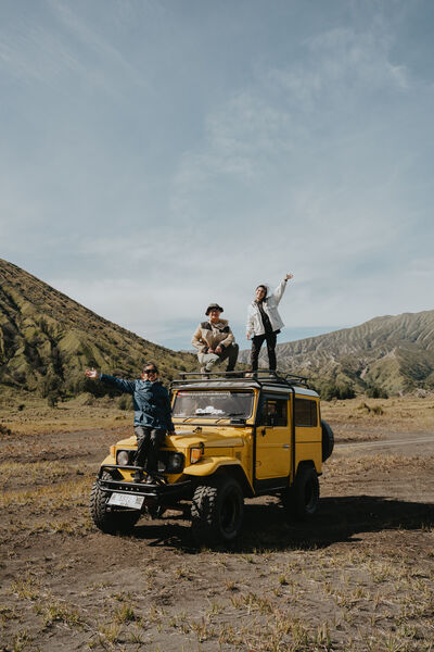 Group of hikers celebrating on an off-road jeep in a rugged Indonesian mountain valley under cloudy skies