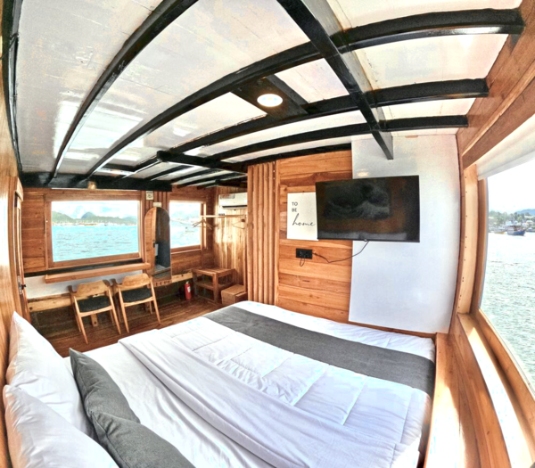 Phinisi master cabin with bed, pillows, TV wall feature and side windows showing open sea on a 3D2N private Komodo cruise, Labuan Bajo