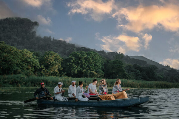 Seated group travelling by boat across a calm waterway in Bali at golden hour, with green hills in the distance