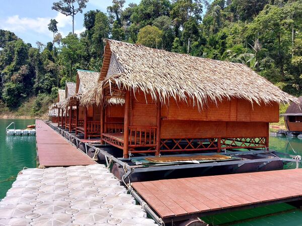 Thatched-roof wooden floating bungalows and moored long-tail boats along a pier on a lake in Thailand
