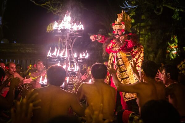 Ornate Indonesian dancer in red-and-gold costume performs in front of a blazing torch display as the crowd watches in Indonesia