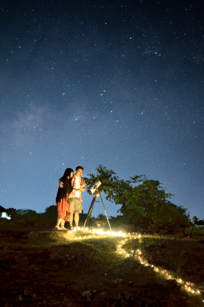 Child and adult seated by a telescope-lit path in Bali, looking up at the Milky Way during a stargazing night