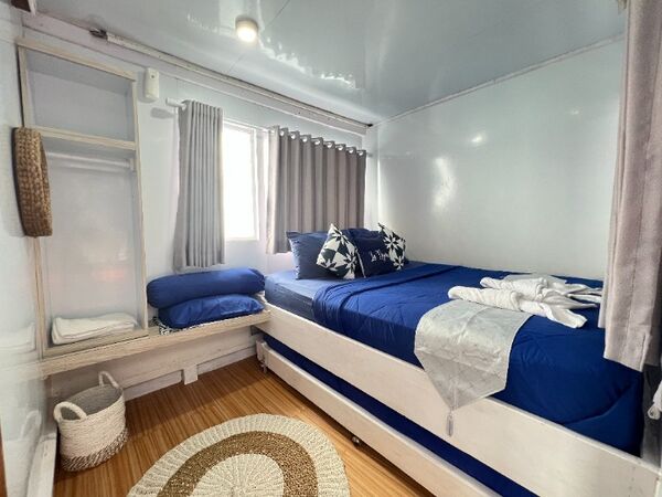 Blue-and-white cabin with neatly made beds and curtains for a cosy 2D1N shared boat trip to Komodo Island