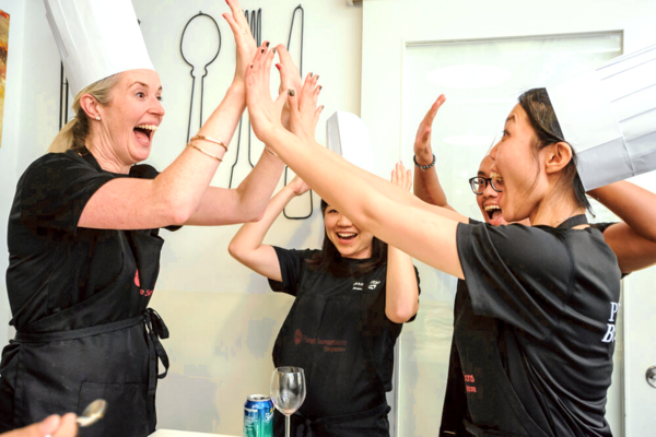 Hands raised in laughter with fellow cooks at Palate Sensations SG after a team MasterChef challenge for workshops in Singapore