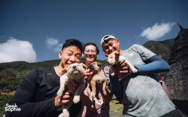 Group posing with small dogs on a viewpoint above the coastline during a Komodo adventure in Labuan Bajo