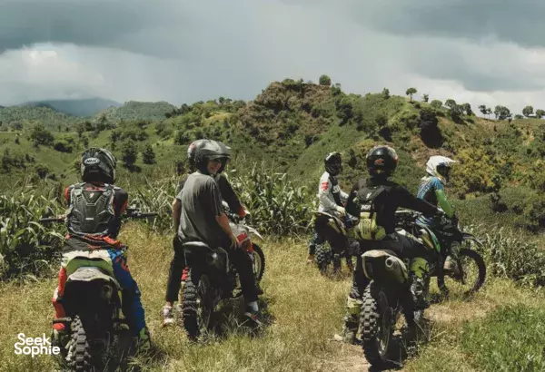Helmeted riders follow a grassy single-track through hills on Lombok during a beginner off-road dirt bike lesson