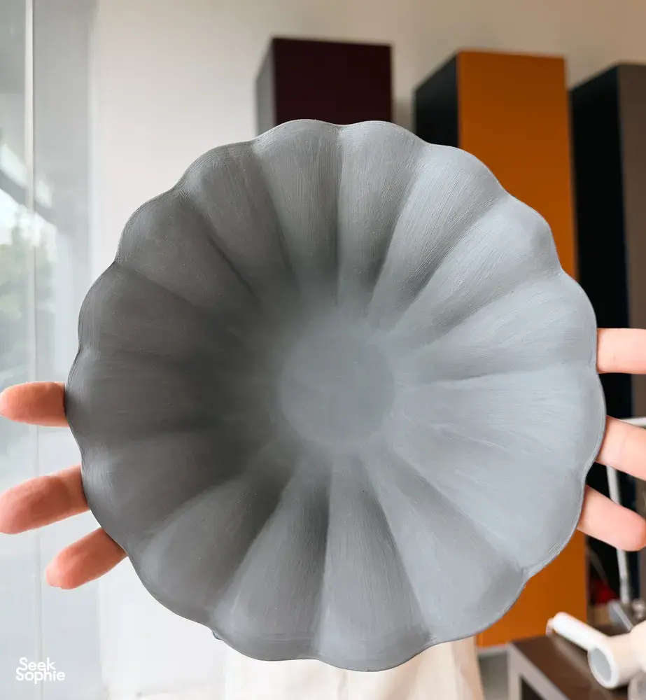 Hands holding a European-style ceramic plate form with a scalloped rim in a Singapore pottery studio