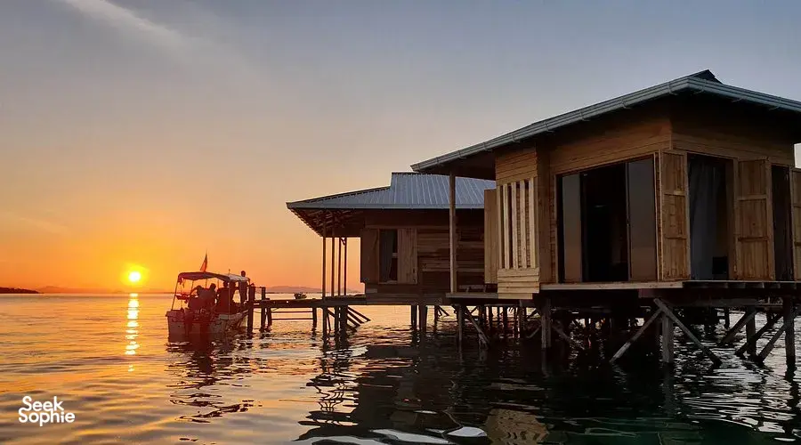 Overwater wooden cabins on stilts at sunset in Semporna, forming a quiet sea lodge along the calm horizon