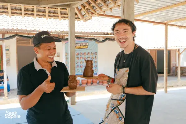 A host and local artisan smile while presenting a small clay piece at the Yogyakarta pottery village during a guided craft session