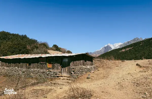 Wooden mountain camp hut overlooking distant peaks during a guided hike to Jade Dragon Snow Mountain from Lijiang