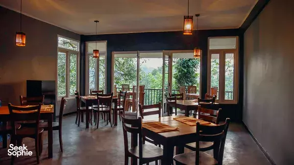 Dining area with wooden tables and chairs at Old Frankland Tea Estate in Kandy, with wide windows opening onto tea gardens