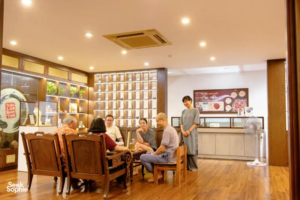 People seated at wooden tables in a bright Hanoi aroma gallery while an attendant stands by a display board