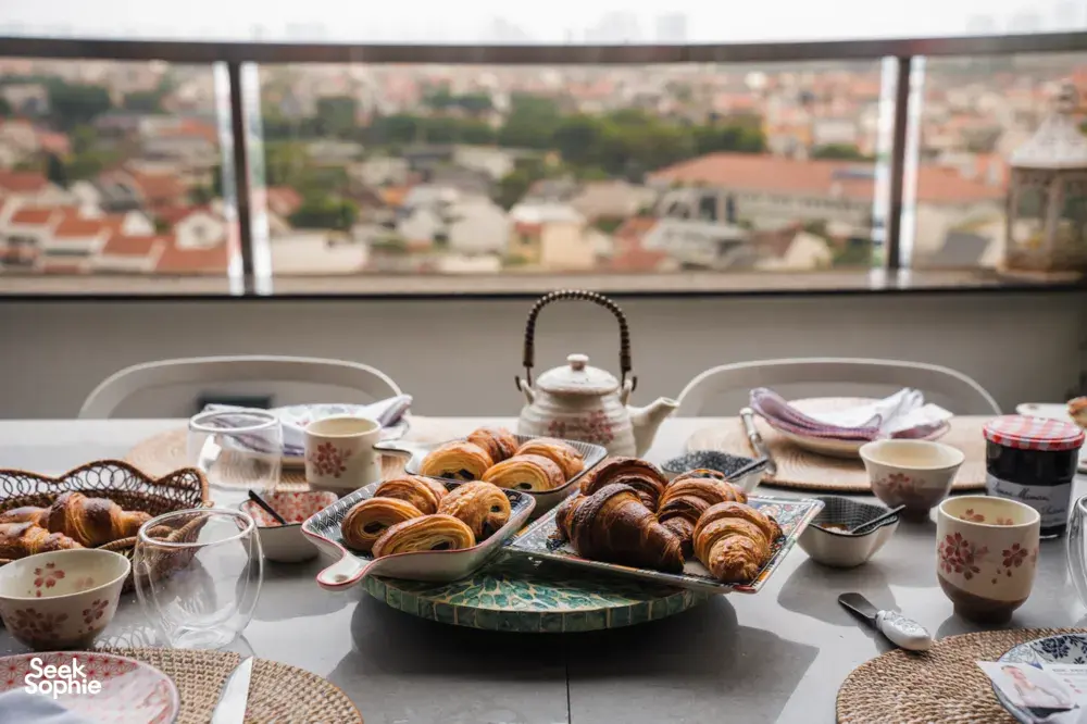 Tray of freshly baked croissants and tea cups on a dining table by a window overlooking Singapore city views