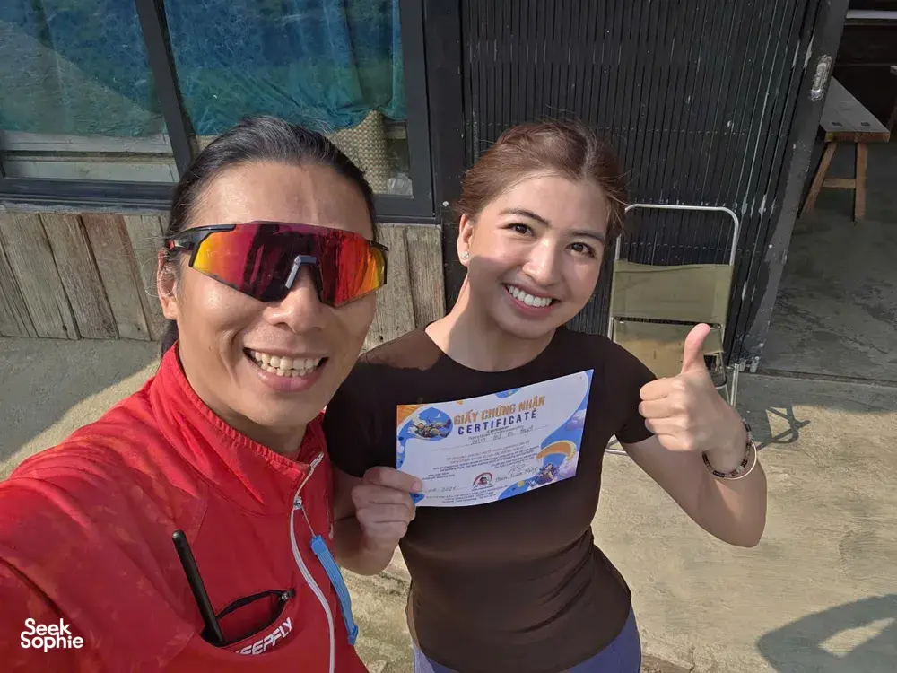 Two paragliding participants smiling and holding a flight certificate at the launch area, ready to fly in Sapa