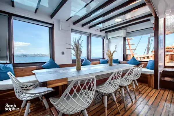 Private 3D2N Komodo cruise on a sleek white phinisi: bright lounge with dining table, sofas and windows overlooking Labuan Bajo