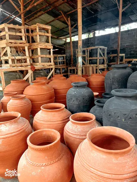 Rows of terracotta and dark-glazed ceramic jars inside a Yogyakarta pottery workshop, displayed among wooden shelves and tools