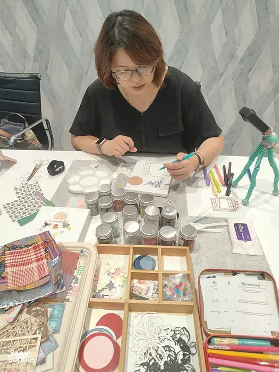 A participant adds details to her vision board for gemstones in Singapore, surrounded by collage templates, pens and jars; workshops in Singapore