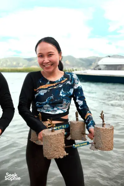 Smiling participant holds cement coral plugs as others plant reefs with Rinca Coral Nursery Program during Komodo day trip in Labuan Bajo