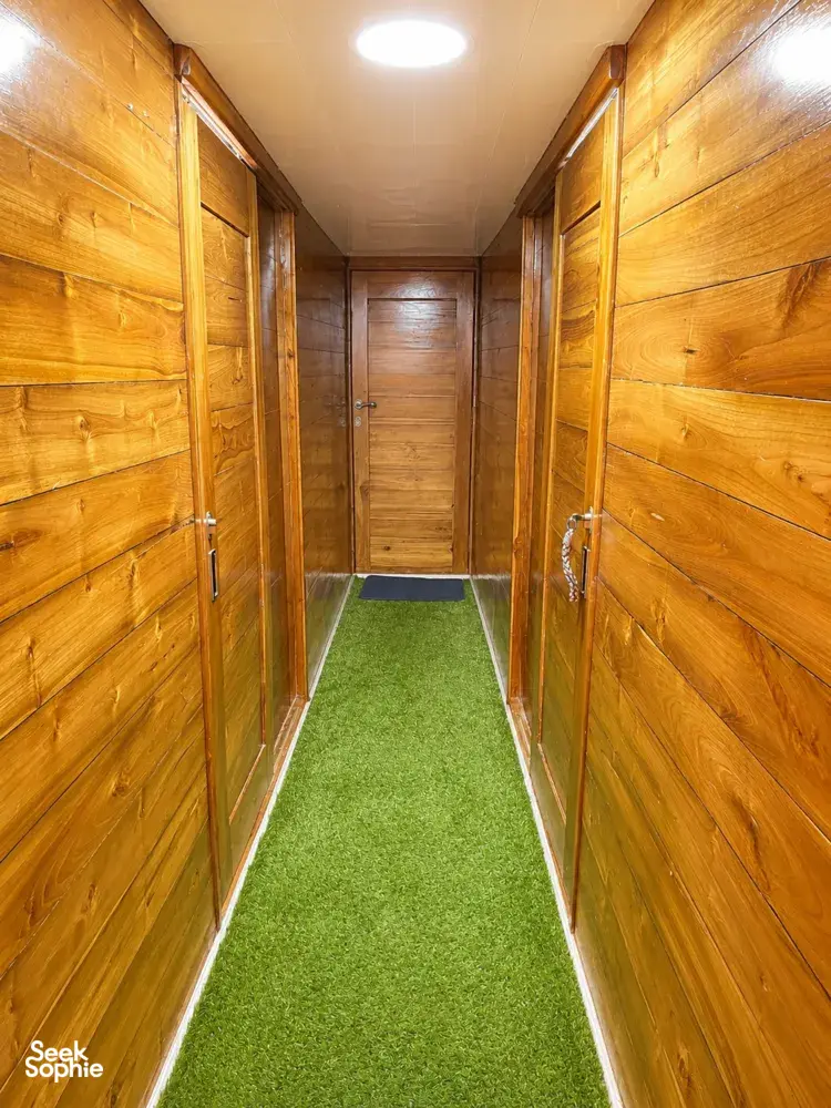 Wooden phinisi corridor with green carpet inside a 3D2N shared cabin on a Labuan Bajo cruise to Komodo Island