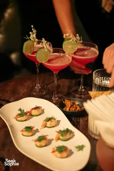 Red cocktails garnished with lime slices and served beside appetisers during the Hoi An cocktail tour