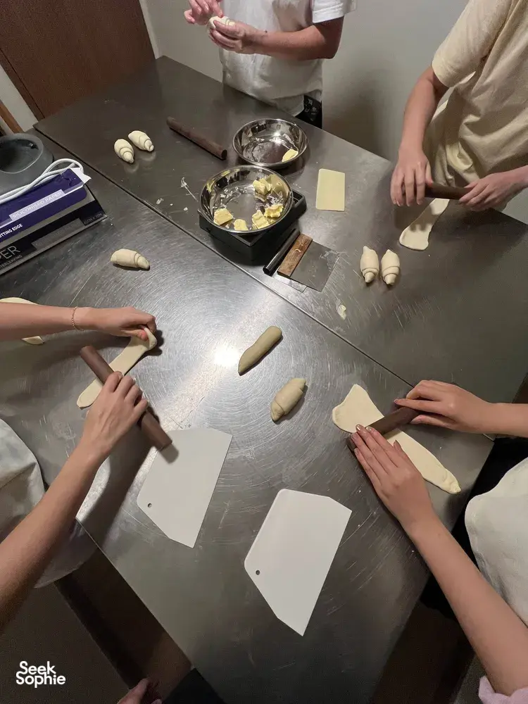 Hands shaping small dough pieces and rolls around a shared workspace at a shio pan baking workshop during workshops in Singapore
