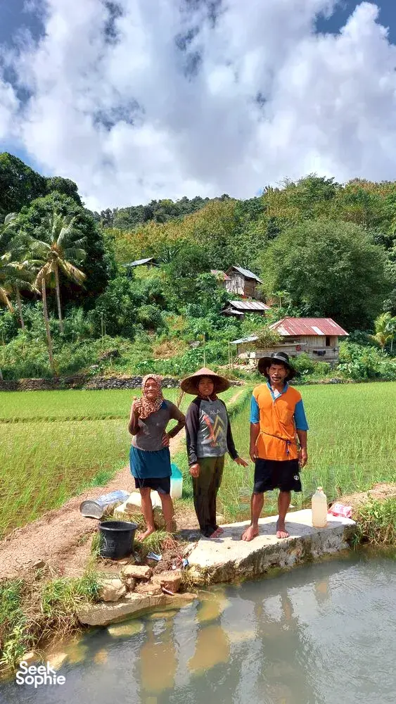 Tiga pengembara berdiri di tepi saluran air kecil di tengah kehijauan bakau yang rimbun dan rumah-rumah berhampiran Labuan Bajo