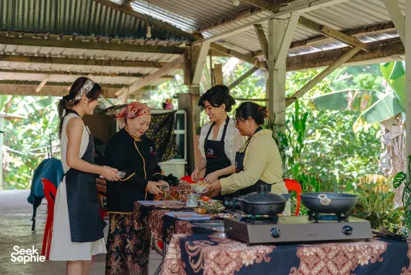 Local family and guests cooking and tasting near a bubbling pot on an outdoor table at an Indigenous Sabahan experience in Kota Kinabalu