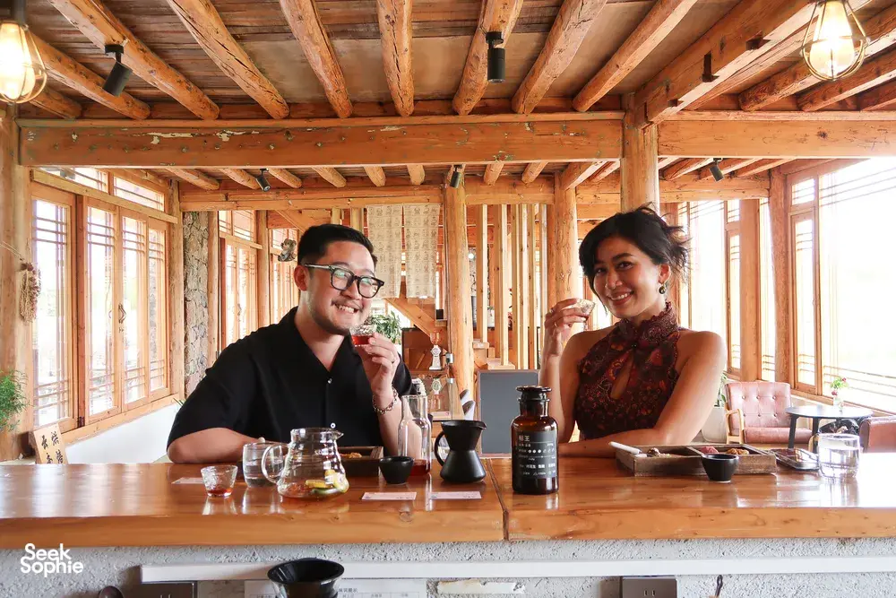 Rustic Lijiang coffee tasting at a family workshop, two guests smiling as they sip from cups beside pour-over brewers