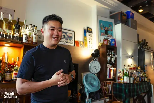 Scotch & Sambal host in a Singapore home bar smiles with a whisky glass, leading a small-batch tasting with bottles behind