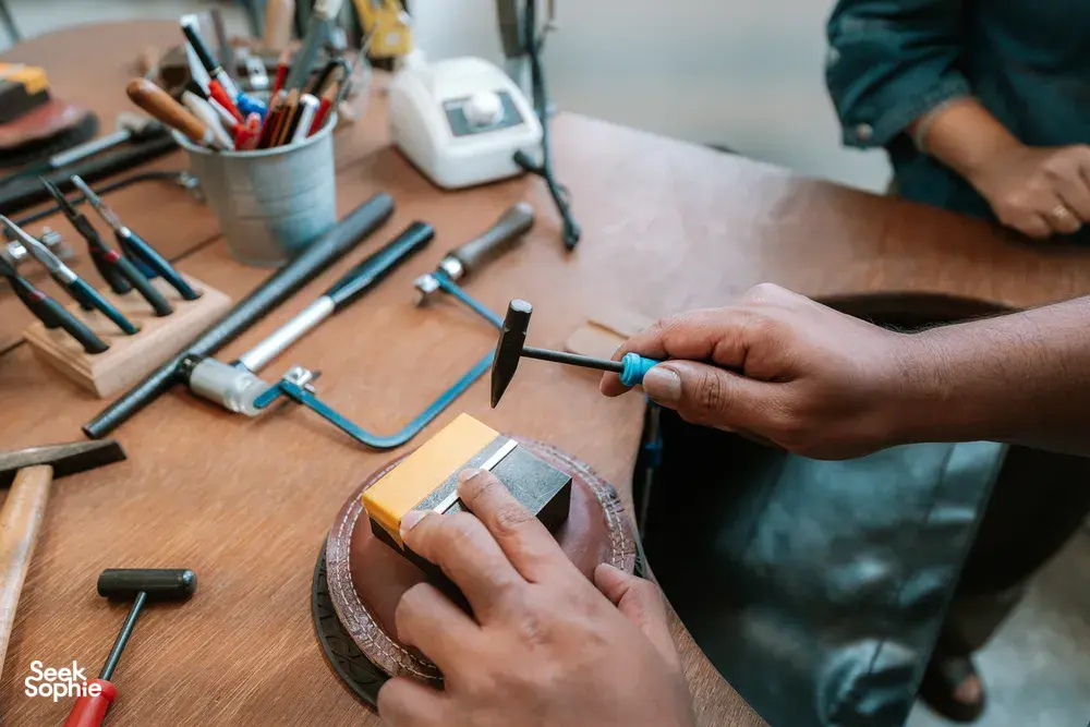 Hands shaping a silver ring with metal tools on a wooden bench at Fat Anvil Studios in Singapore â workshops in Singapore