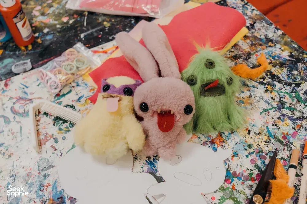 Ugly-cute plushie keychains in progress on a colourful craft table in Singapore, with felt pieces and scissors