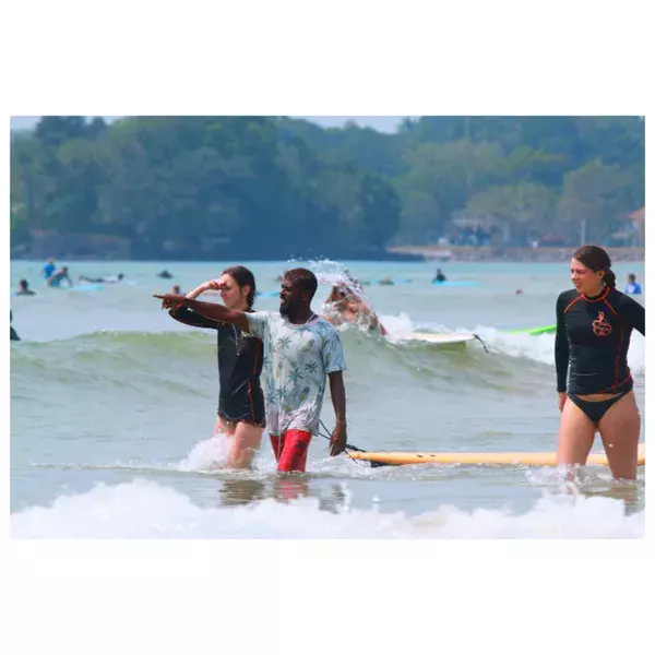 Surfers wading into the waves at Weligama Bay, with foam and boards at a group surf lesson on a bright day