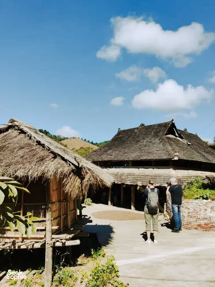 Wisatawan berjalan melewati rumah beratap jerami khas Dai di jalur halaman terbuka saat perjalanan sehari privat di Xishuangbanna