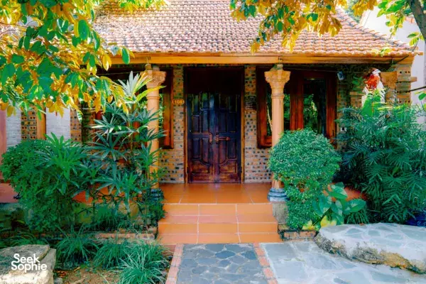 Tiled entry path framed by potted plants leading to a brick-and-wood house at Lovely Village Homestay, Ninh Binh