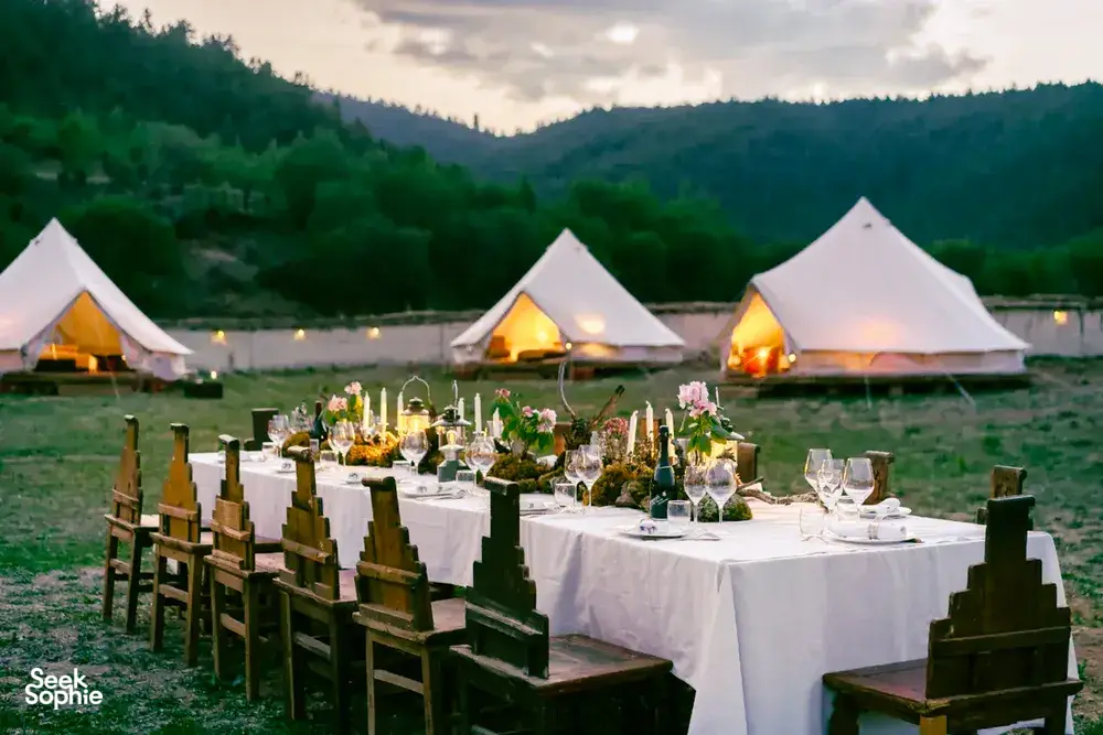 Shangri-La mountain valley camp dinner with set dining table in front of lit white tents at dusk, Mission Liotard stay