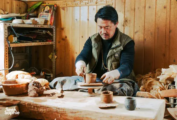 Pottery workshop in Shangri-La with a potter shaping clay on a worktable, surrounded by tools and ceramics