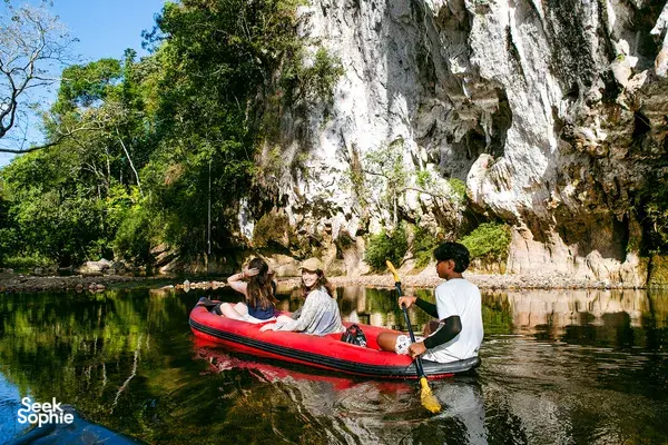 People relaxing in a red boat on Cheow Lan Lake, paddling past limestone cliffs at Khao Sok