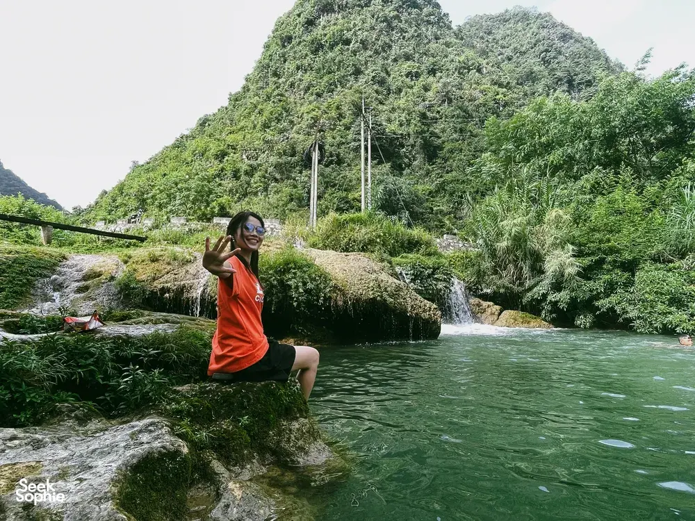 Traveller relaxing on a river rock by a waterfall in Cao Bang, Vietnam, amid lush green jungle on a motorbike loop